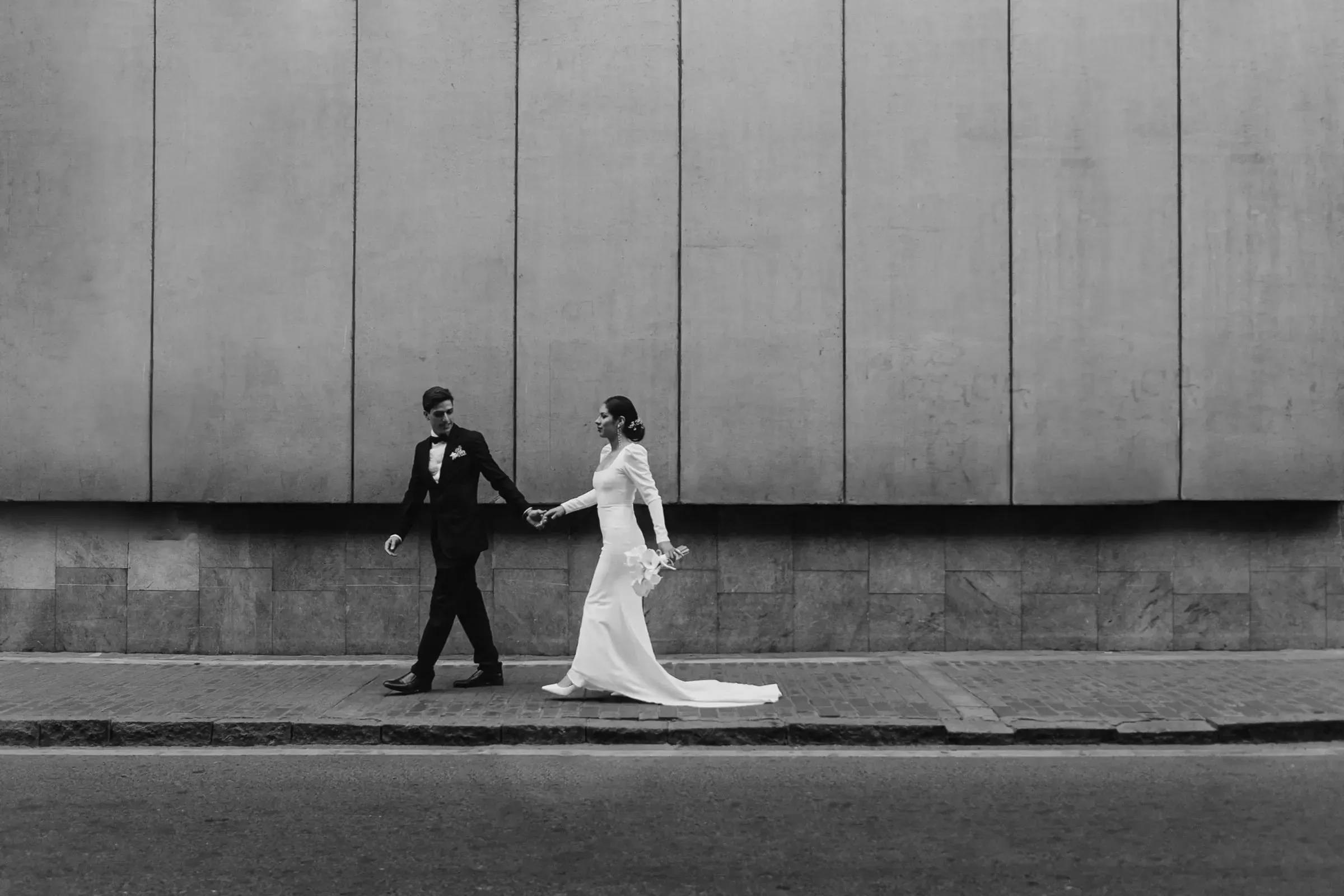 Bride and groom walking along a city street, in black and white.